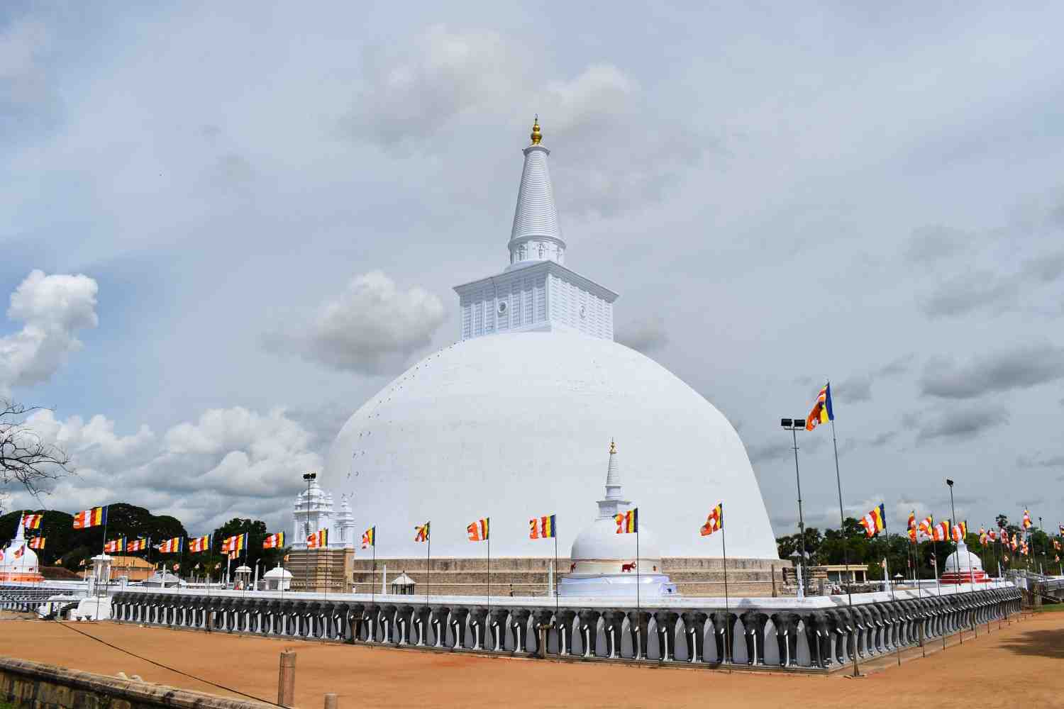 A large white stupa stands majestically against a cloudy sky, showcasing the beauty of Sri Lankan temple architecture.&nbsp;