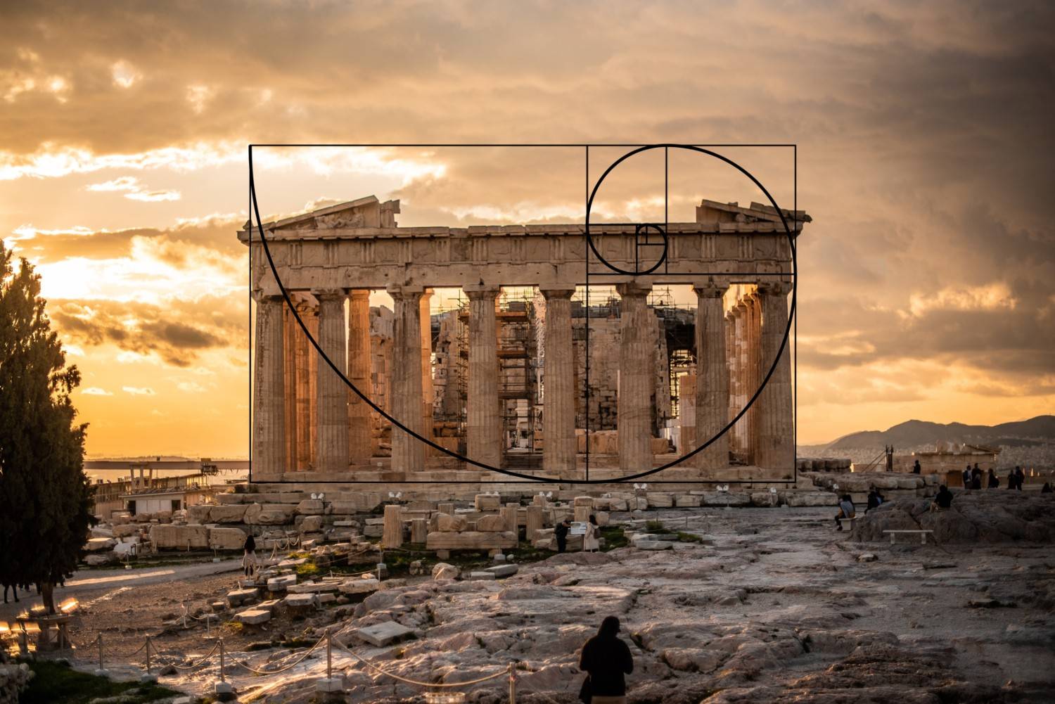 The image shows the Parthenon in Athens during sunset with a cloudy sky. A golden spiral overlay, reminiscent of sacred geometries, highlights the architectural proportions.&nbsp;