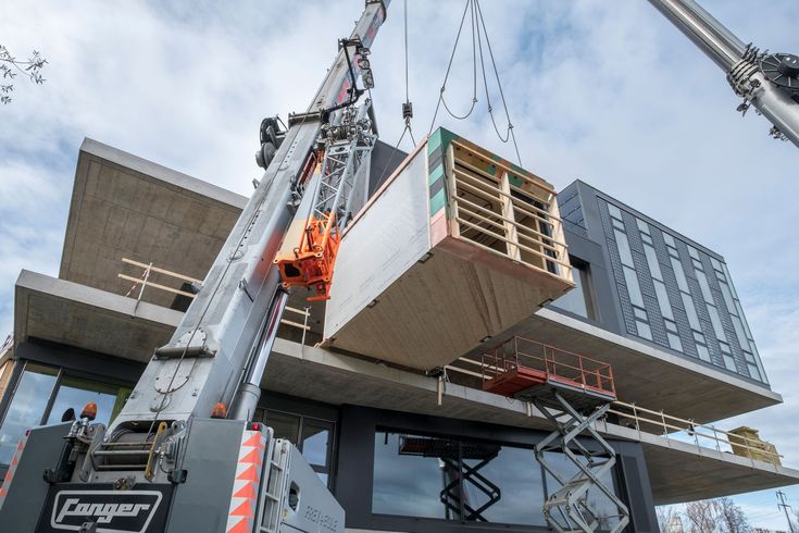 A crane lifts a large construction module into place on a modern building site, showcasing the precision of BIM prefabrication.