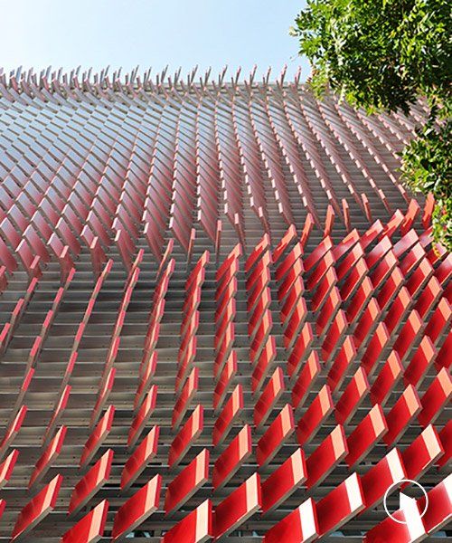 A modern architectural facade, crafted with careful material selection, features red, angled fins creating a dynamic pattern against a clear blue sky. 