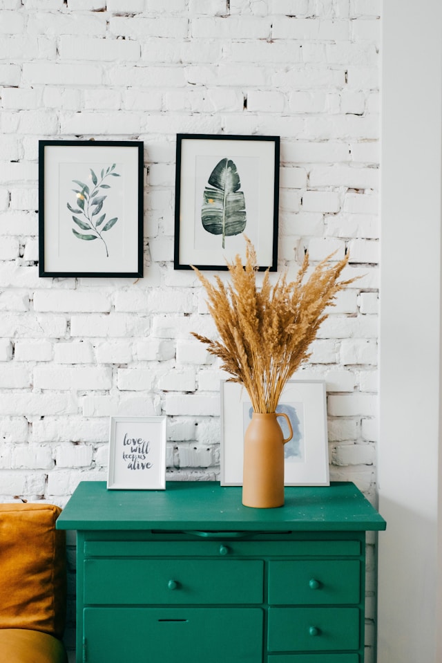 A cozy interior features a green dresser against a white brick wall, showcasing effective interior decoration. 