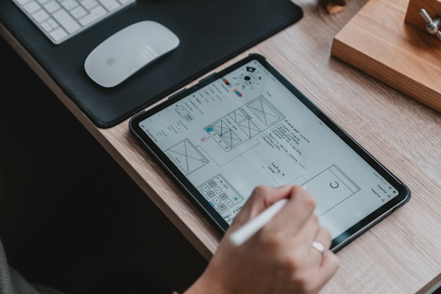 A person is using a stylus to design a UI-UX wireframe interface on a tablet. 