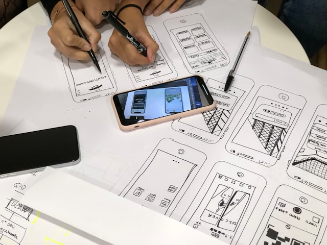 Designers are working on a mobile app project, drawing wireframes and UI sketches on paper. 