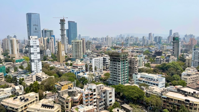 Aerial view of a sprawling urban landscape with numerous residential and commercial buildings. Skyscrapers rise in the background, while densely packed, architecturally compliant mid-rise buildings fill the foreground. 