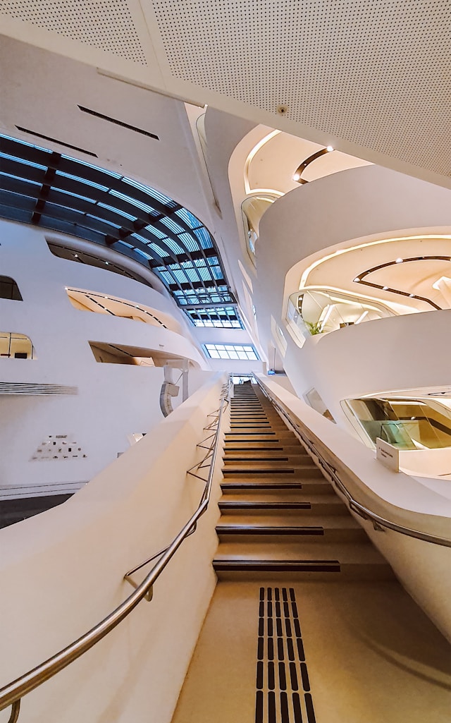 Wide-angle view of a modern interior with sweeping, curved white walls and staircases leading upward. Glass panels on the ceiling allow natural light to illuminate the space, emphasizing its eco-friendly architecture and creating a futuristic and open atmosphere.