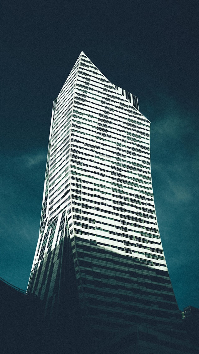 A striking, twisting skyscraper against a teal sky showcases Rhino Architecture at its finest. The building's glass facade reflects light, emphasizing its modern, angular design created with Grasshopper Software. 