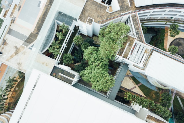 Aerial view of a modern architectural complex with white buildings, greenery, and a curving pathway. This sustainable architecture seamlessly blends urban structures and planted trees, creating a harmonious integration of nature and design.