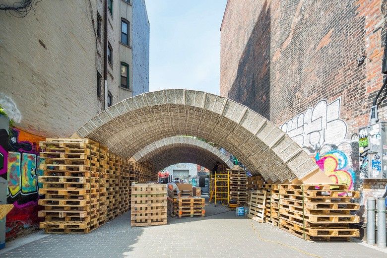 A large archway constructed from stacked blocks stands in an urban alleyway, showcasing sustainable practices—an ode to the circular economy in the construction industry.