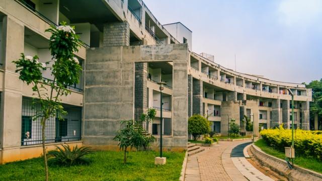 A modern, multi-story concrete building with balconies showcases elements of global styles, surrounded by greenery.&nbsp;