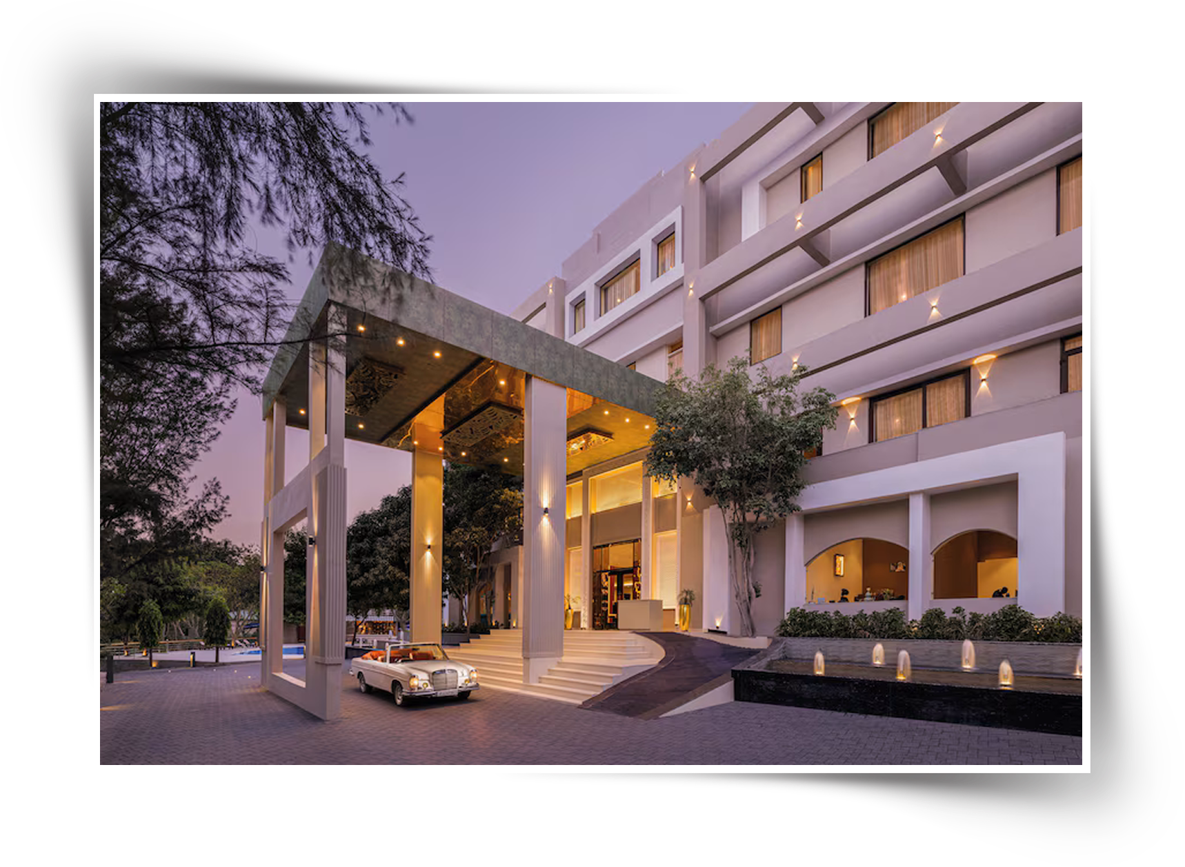 Modern hotel entrance porch with tall columns, warm ambient lighting, landscaped driveway, and luxury car at the drop-off area.