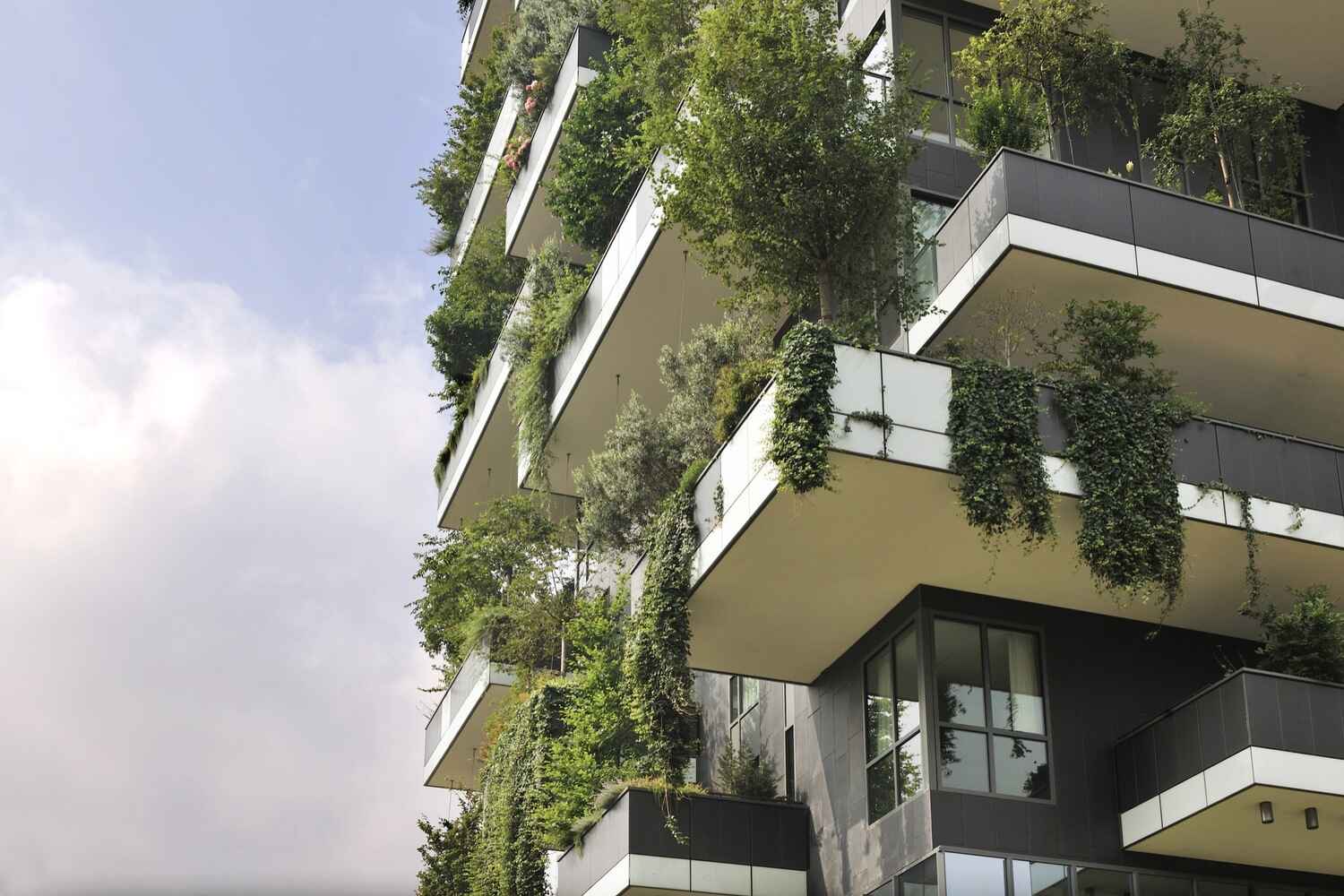 An eco-friendly building facade featuring multiple balconies, each adorned with lush green plants and trees. This sustainable architecture seamlessly integrates nature, creating a vertical garden effect. 
