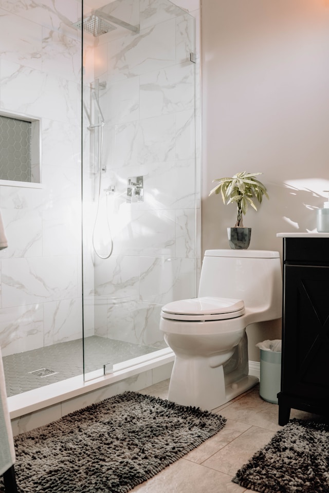 A modern bathroom showcases a glass-enclosed shower with marble tiles. Adhering to accessibility standards, the white toilet with a small potted plant on top complements the black vanity. 