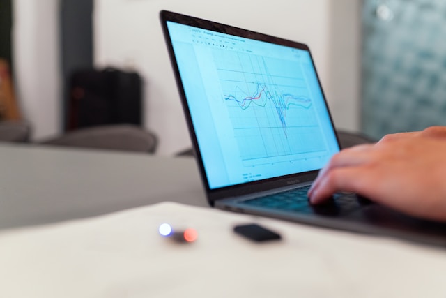 A person is using a laptop displaying a graph with multiple colored lines, showcasing innovative design solutions. The scene includes a blurred background with a few items on the desk, such as papers and small electronic components.