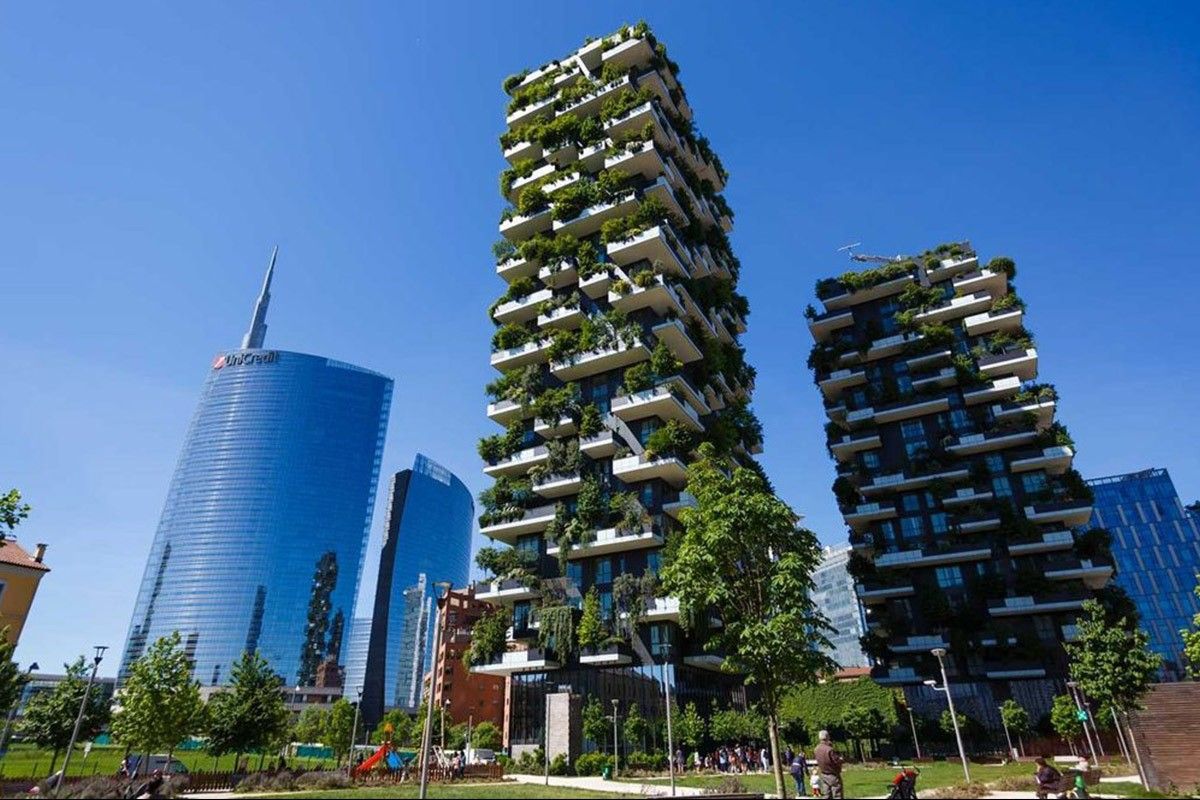 A modern urban scene featuring two vertical forest skyscrapers with lush greenery on balconies highlights sustainable design. Nearby, a sleek, curved glass building complements the eco-friendly materials. A clear blue sky and scattered trees on the ground complete the green architecture.