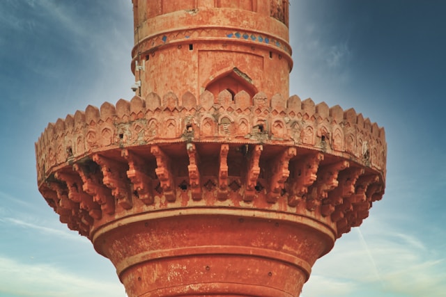 A close-up view of an intricately carved, red sandstone circular balcony on a historical tower, perfect to cover in architectural walks.&nbsp;
