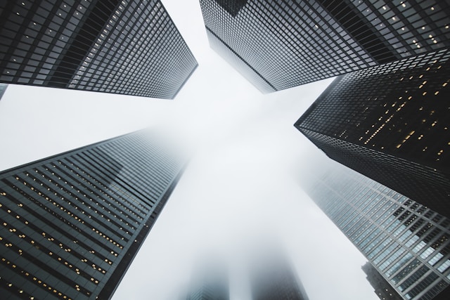 A view looking up at tall skyscrapers on a foggy day, with the tops of the buildings disappearing into the misty sky. 