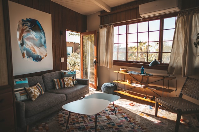 A vastu compliant living room with a gray sofa, colorful cushions, and a white coffee table.&nbsp;
