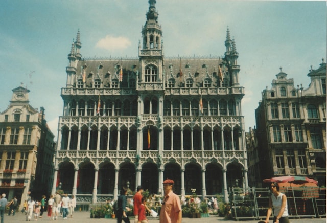 A historical building with intricate Gothic architecture, complete with flying buttresses, stands prominently. The structure features ornate spires and detailed carvings, complemented by ribbed vaults, with a vibrant city atmosphere surrounding it.
