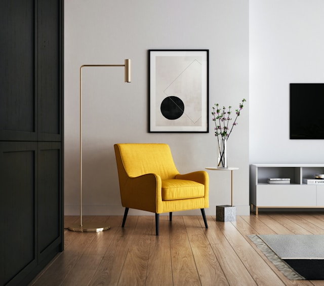 A modern living room with a yellow armchair, tall floor lamp, and small side table with a plant showcases art elements through abstract wall pieces. 
