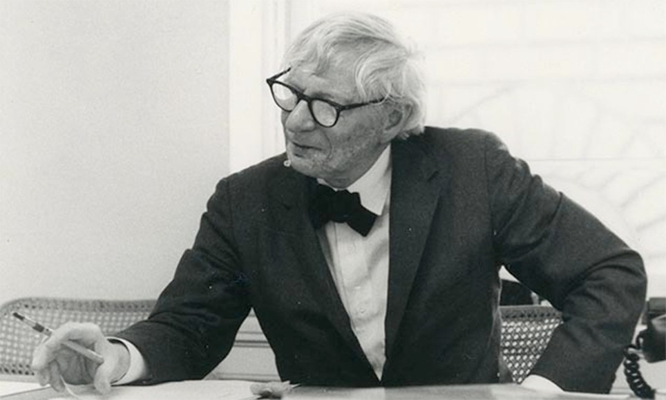 Visionary architect, Louis Kahn sits at a desk with a pen in hand. He appears thoughtful, contemplating form and function study in his designs.