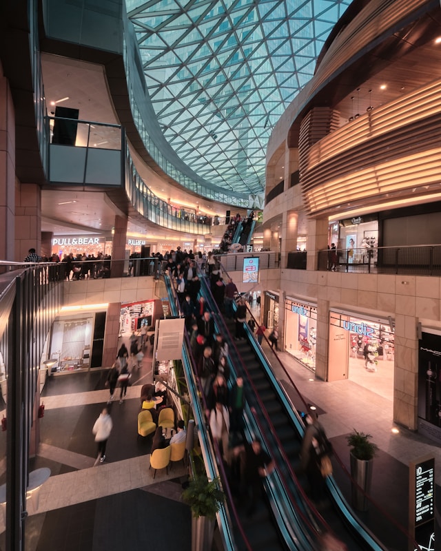 A bustling shopping mall interior with a high, geometric glass ceiling showcases cutting-edge design optimization. 