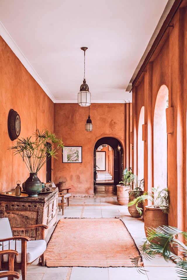 A corridor with terracotta walls features a rug, potted plants, and a wooden console table with decorative items, reflecting Vastu architecture. 