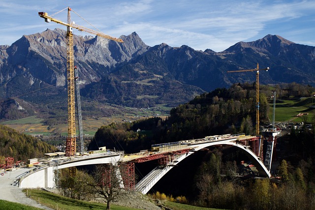 A large bridge stretches across a valley with two towering cranes positioned on each side, showcasing modern BIM Automation in construction. 