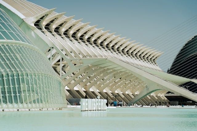 Parametric architecture with white, curved structures and geometric designs reflecting in a calm pool. 