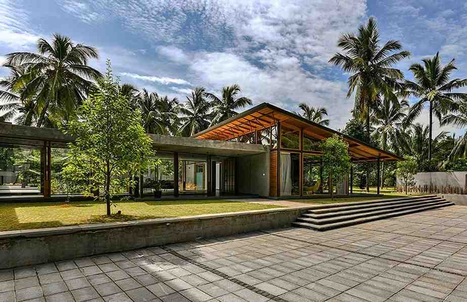 Contemporary building with a wooden roof and glass walls, showcasing sustainable design, surrounded by palm trees and greenery. 