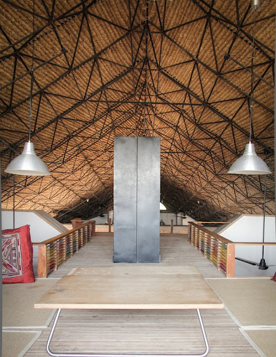 A spacious and rustic attic room with a high, triangular ceiling made of wooden panels supported by dark metal beams, adhering to sustainable architecture principles.