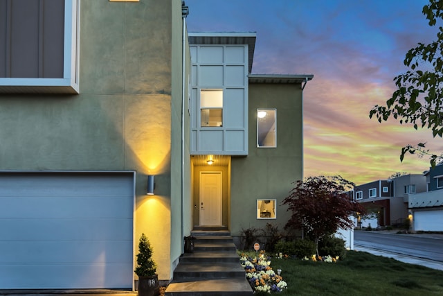 Modern two-story house with a lit entrance, stairway, and garage, designed for positive energy. The facade is complemented by a small tree and flower bed. 